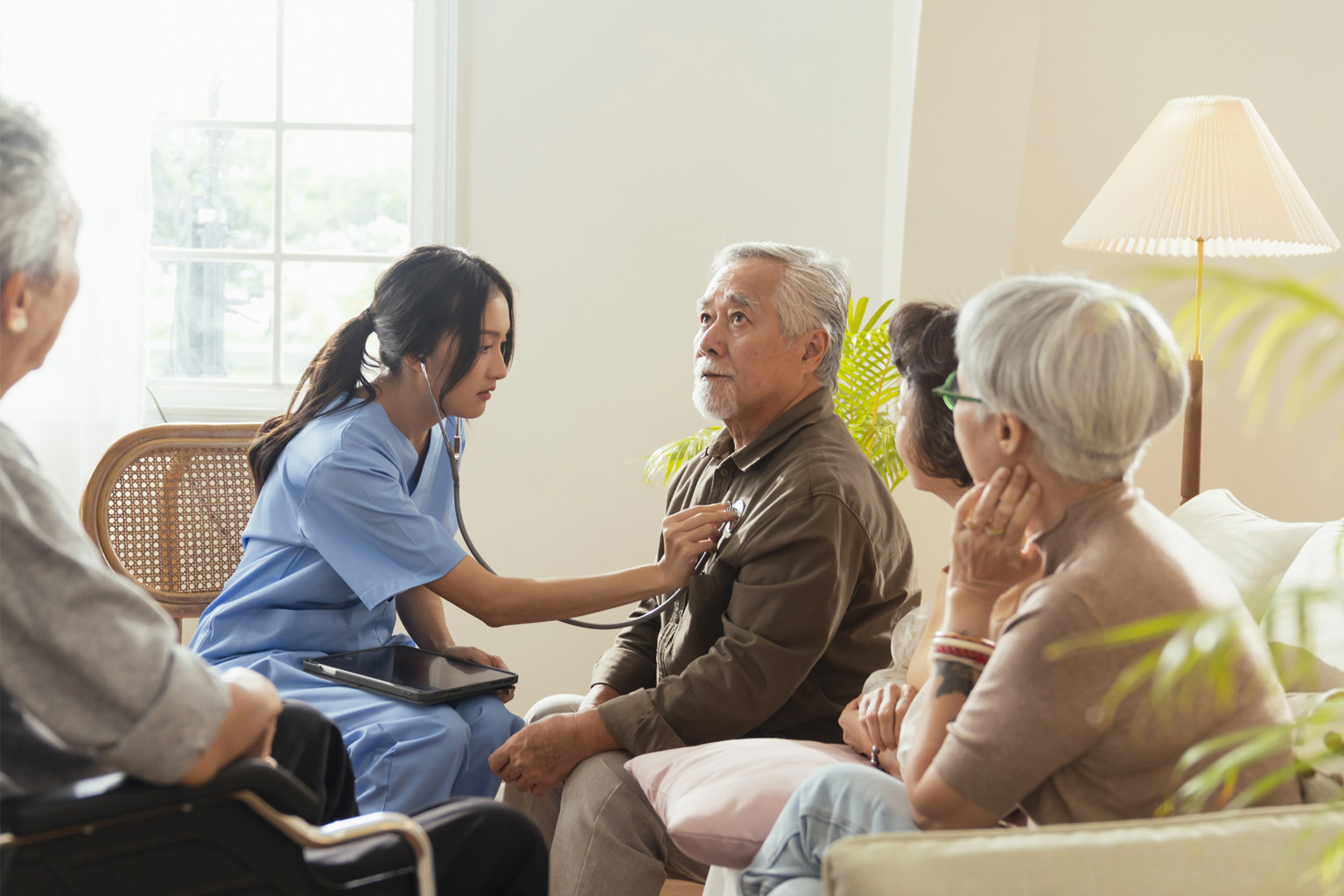 Caregiver checking an elderly resident’s vitals with a stethoscope in a care-home lounge