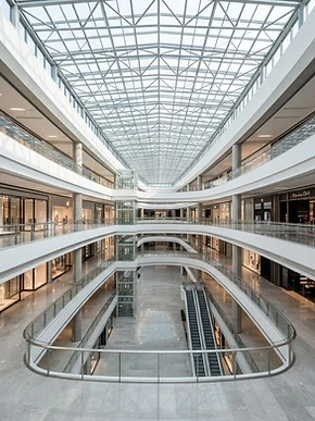 A bright, modern shopping mall atrium with multiple levels of retail storefronts
