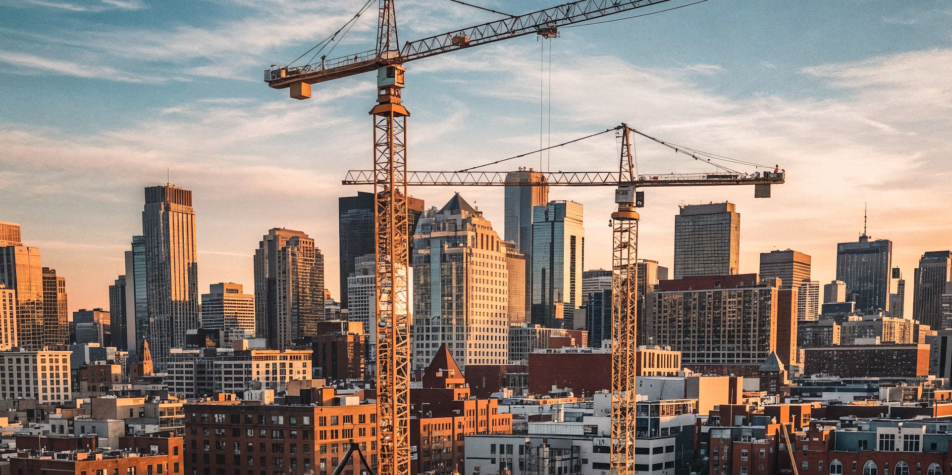 Tower cranes over a city skyline at golden hour