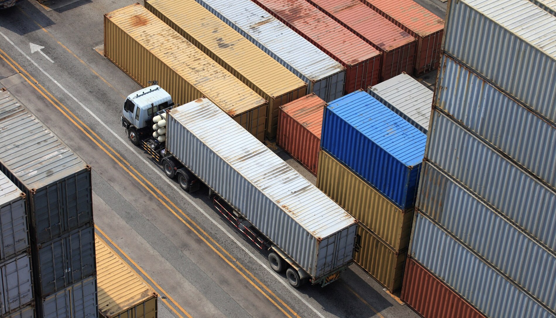 Container yard with a truck hauling a shipping container between stacked containers